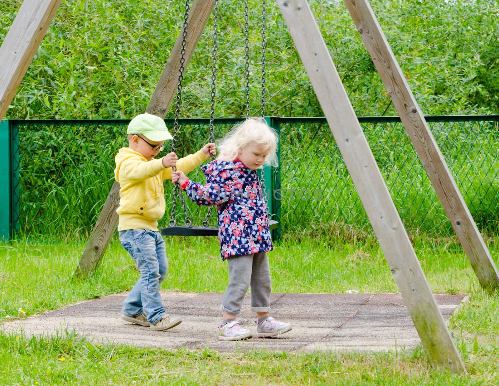 Young children, a boy with a girl swinging on a swing