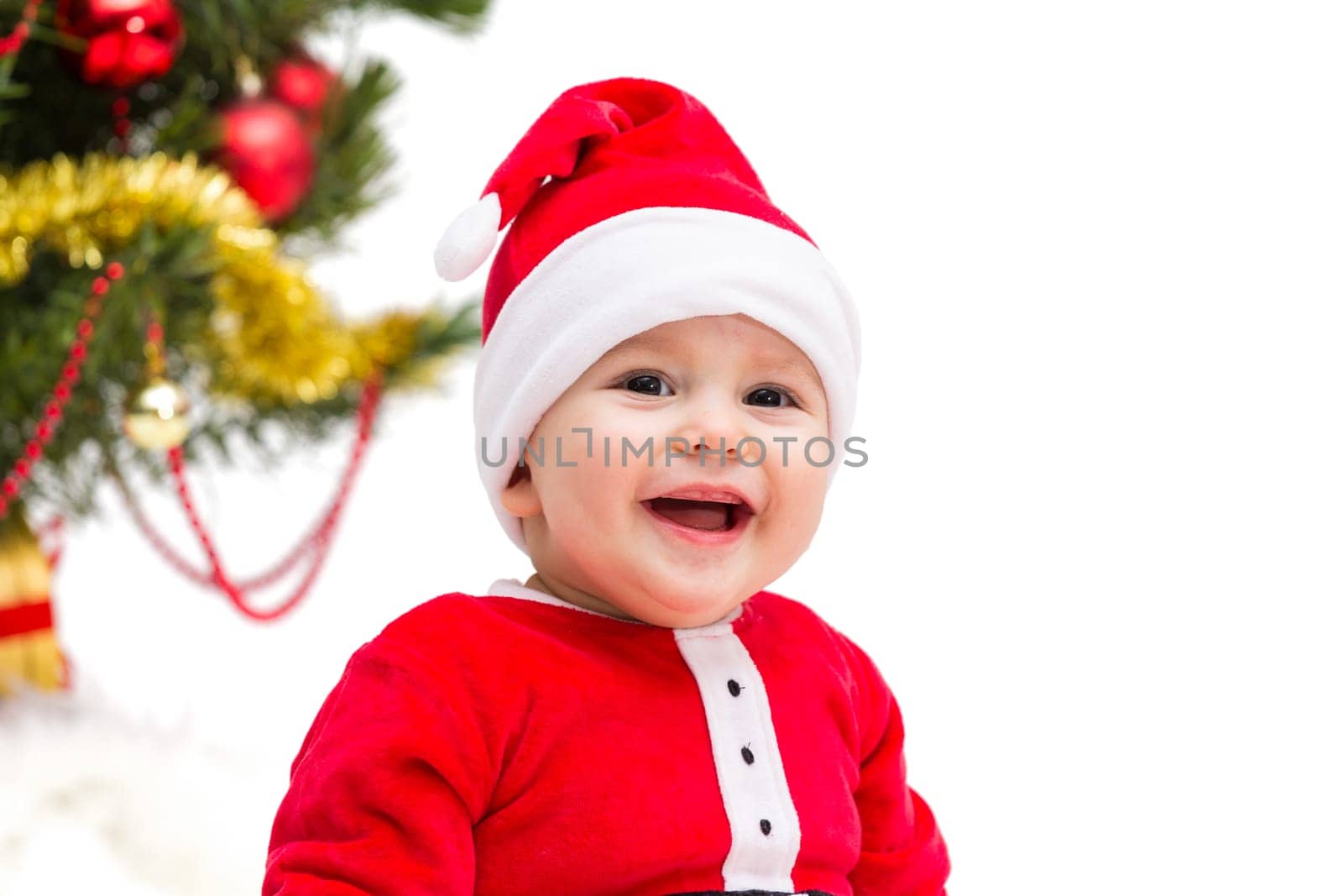 Happy smiling baby wearing a red and white Christmas Santa hat and suit, isolated on a white background.