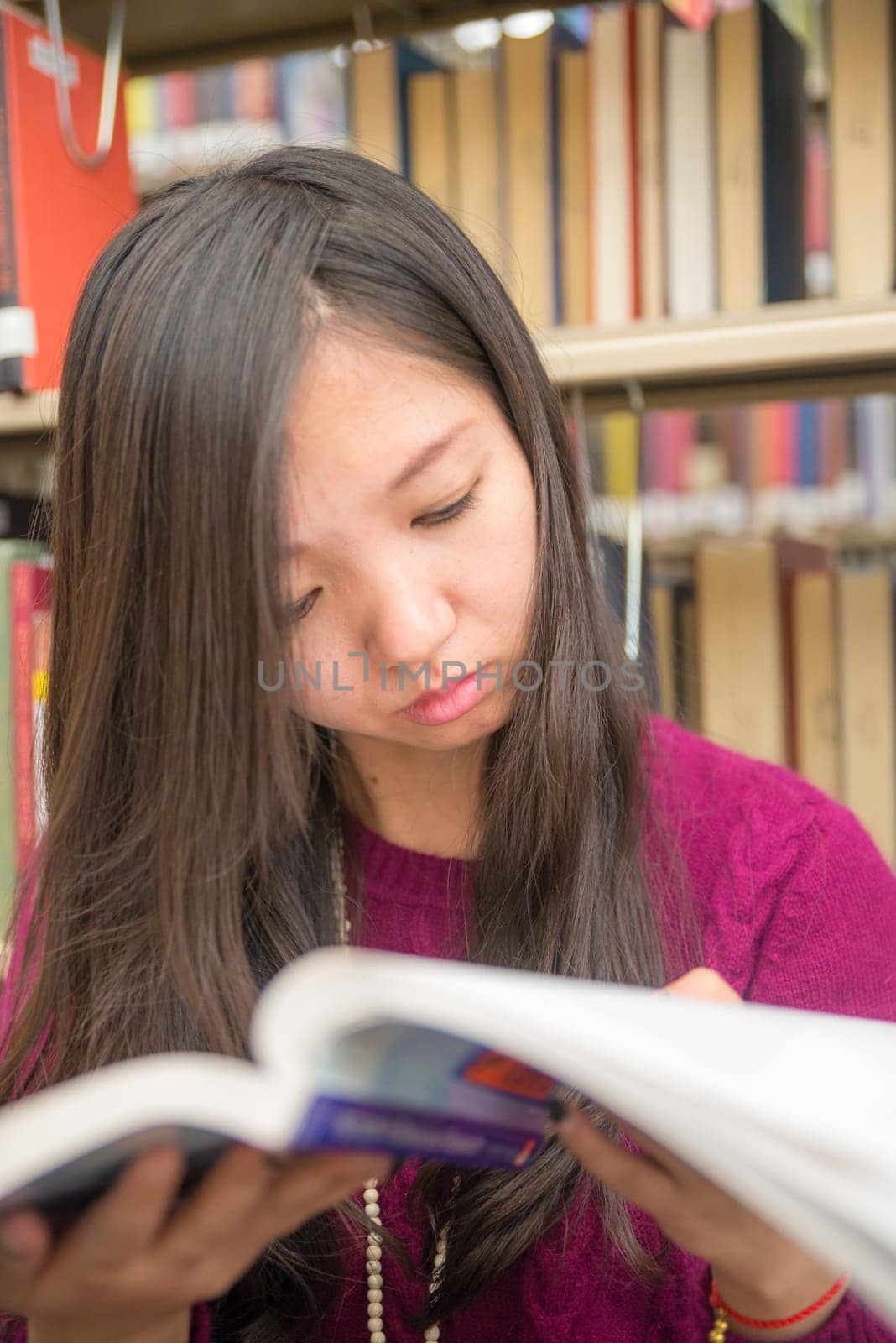 Woman reading a book next to a book shelf in library