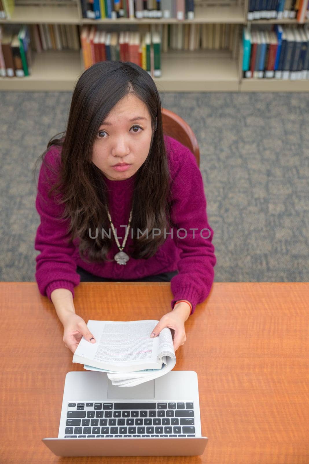 Woman with book and laptob studying in library
