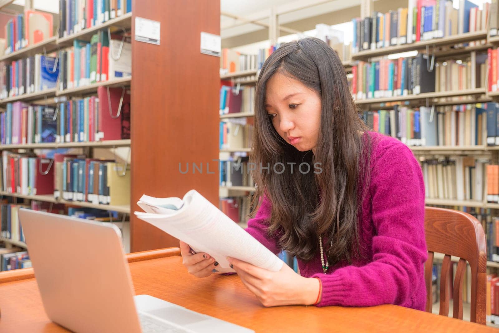 Woman with book and laptob studying in library