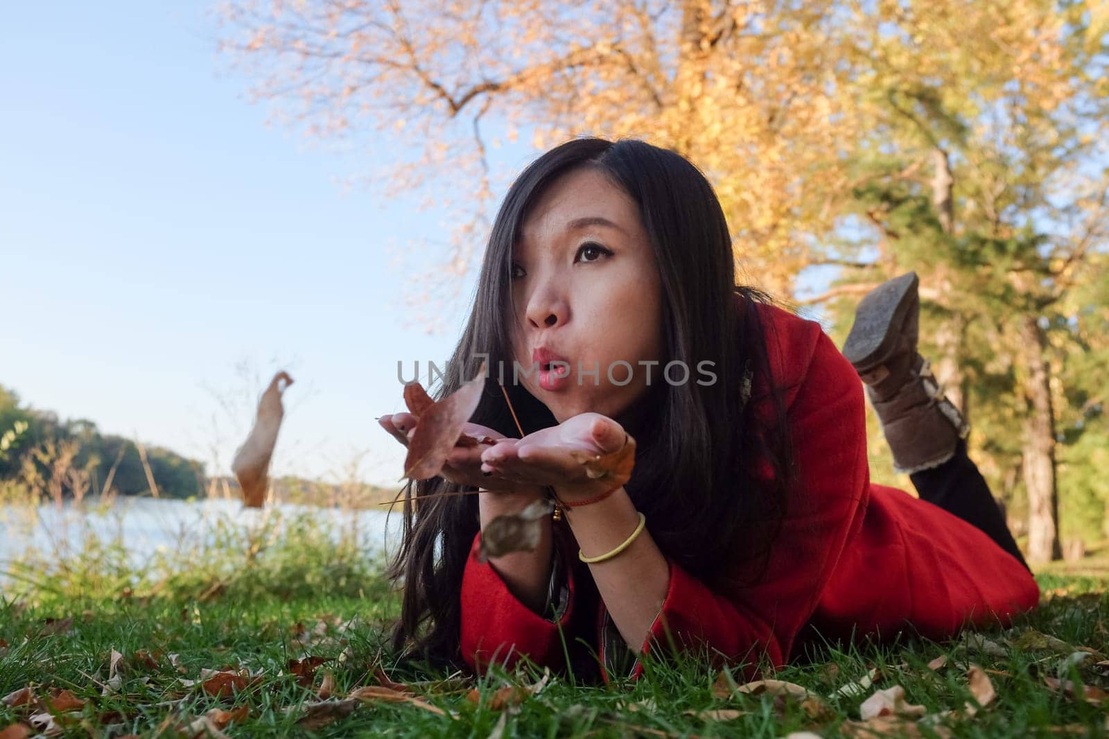 Woman laying on grass blowing away a handful of leaves