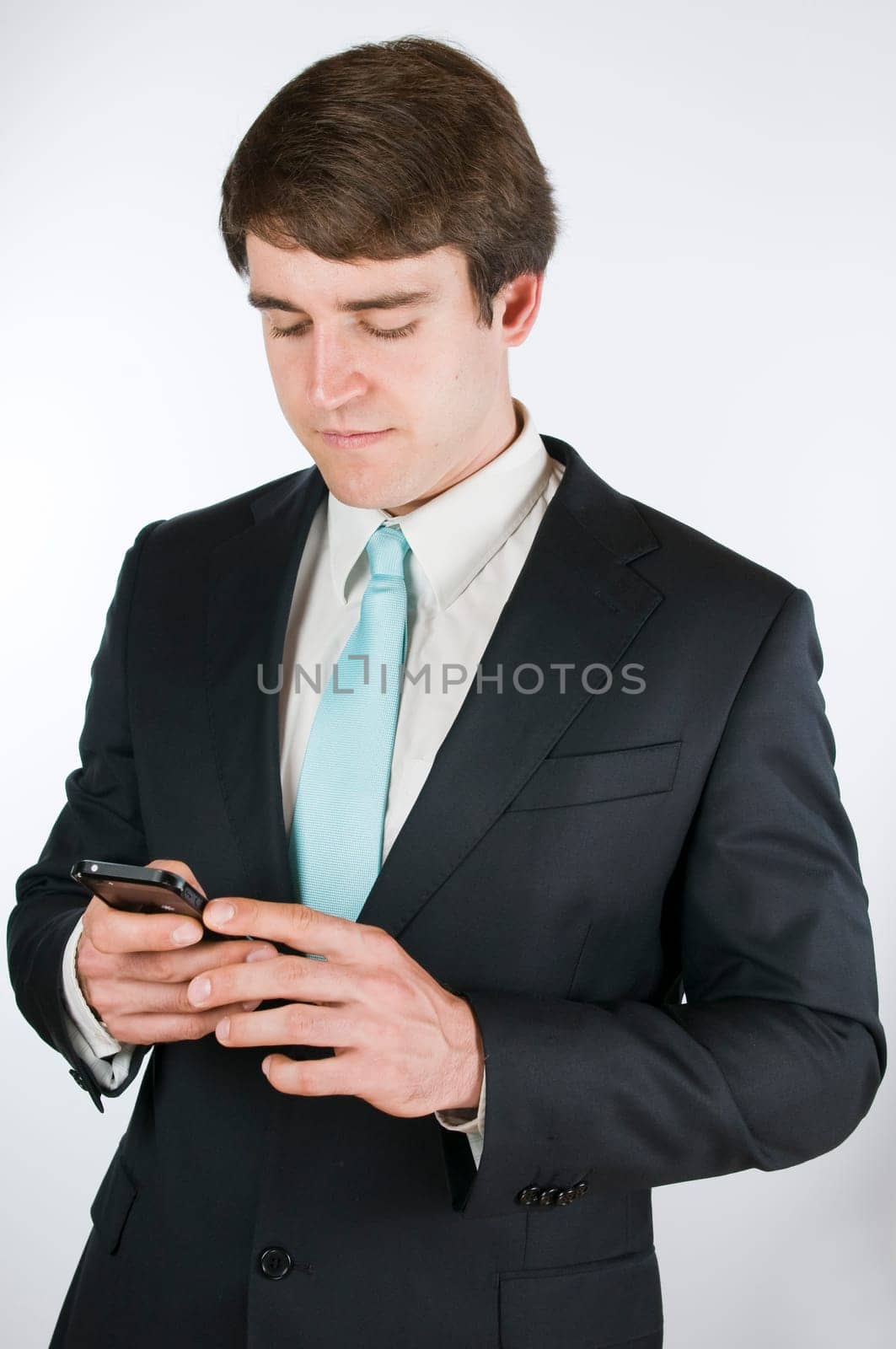 Waist up a young man in a black suit against white background with forward looking holding their smart phone on the display.