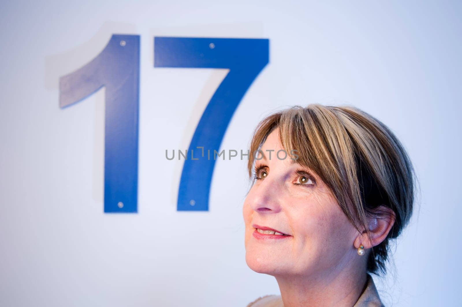 lateral head portrait of a middle-aged man smiling at an angle looking in front of a white wall with the number "17"""