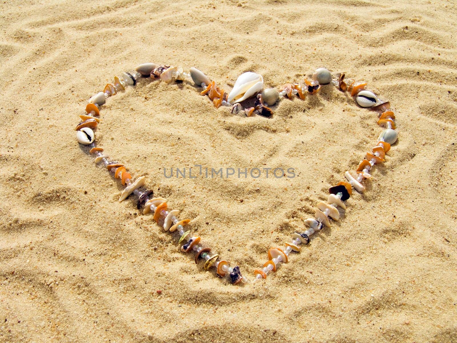Heart from cockleshells and sea pebbles laid out on sand