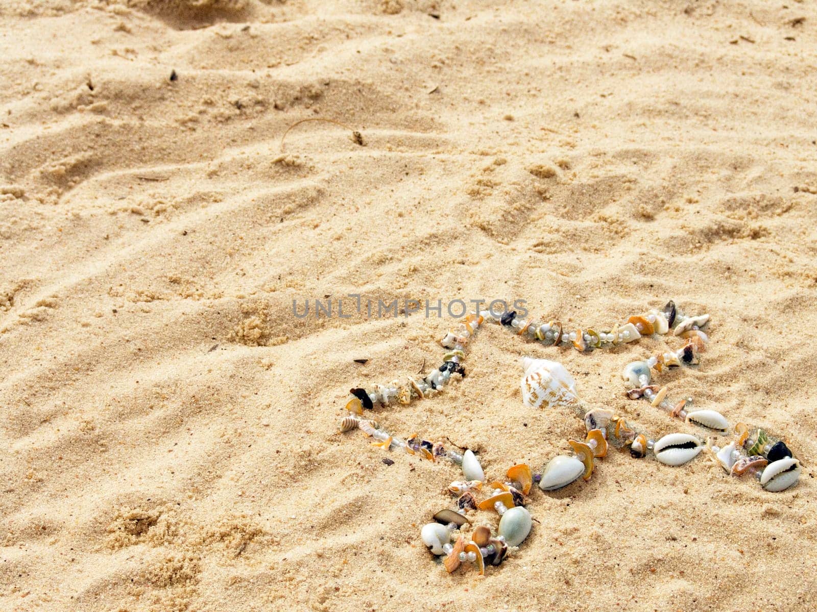 Star from cockleshells and sea pebbles laid out on sand