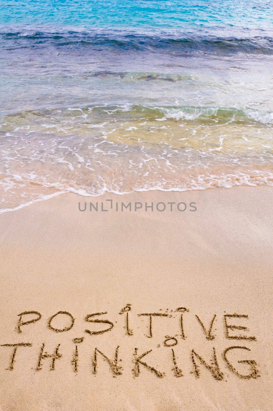 Positive Thinking message written on sand, with waves in background