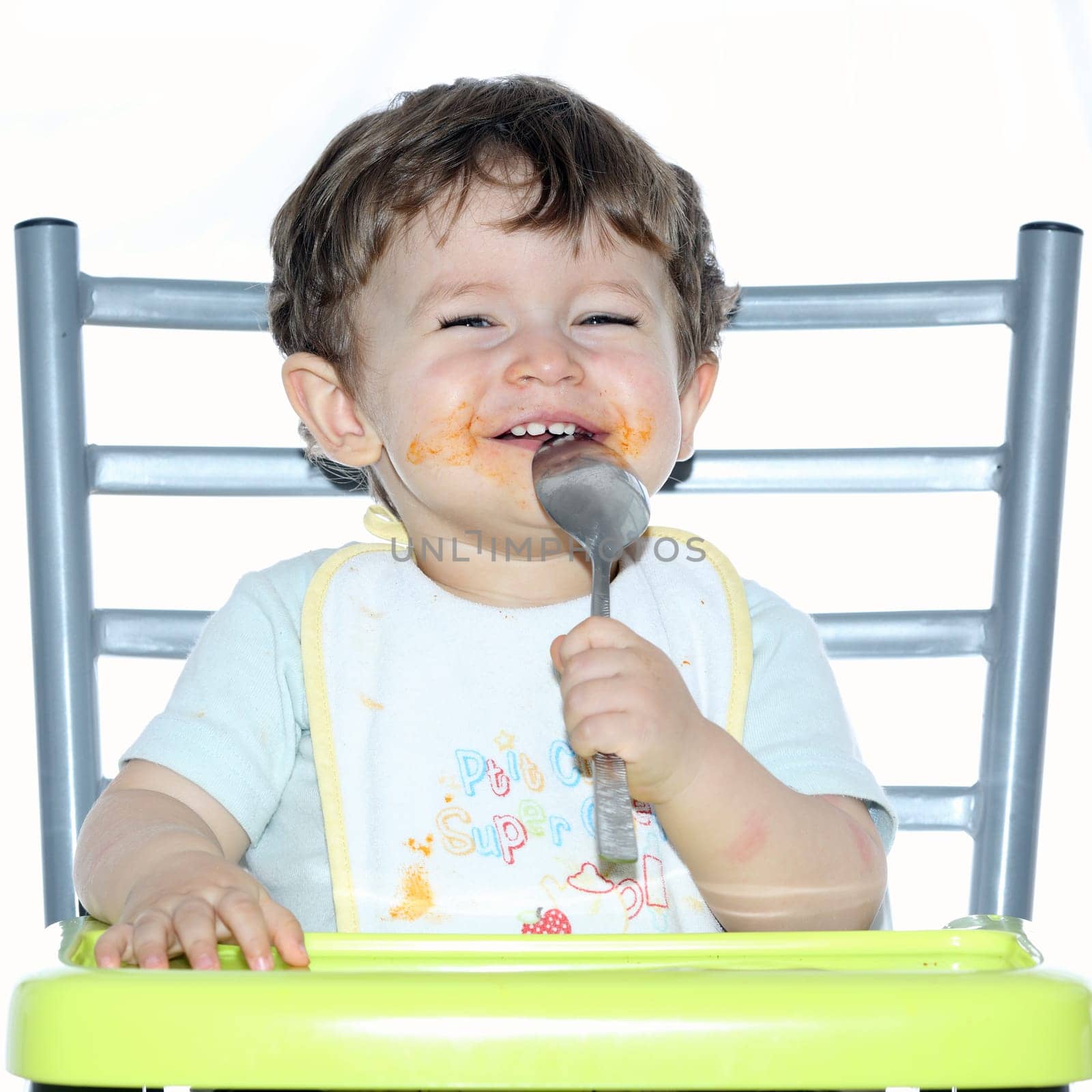 Details of a young boy sitting on a chair and playing with a spoon.