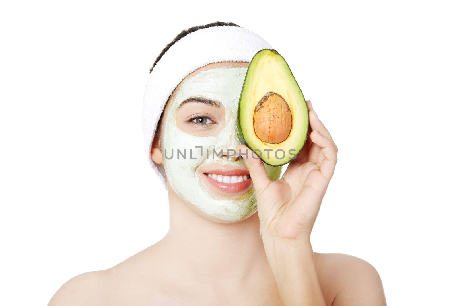 Young woman with a  smile holding avocado heaving face clay mask on the face in a spa