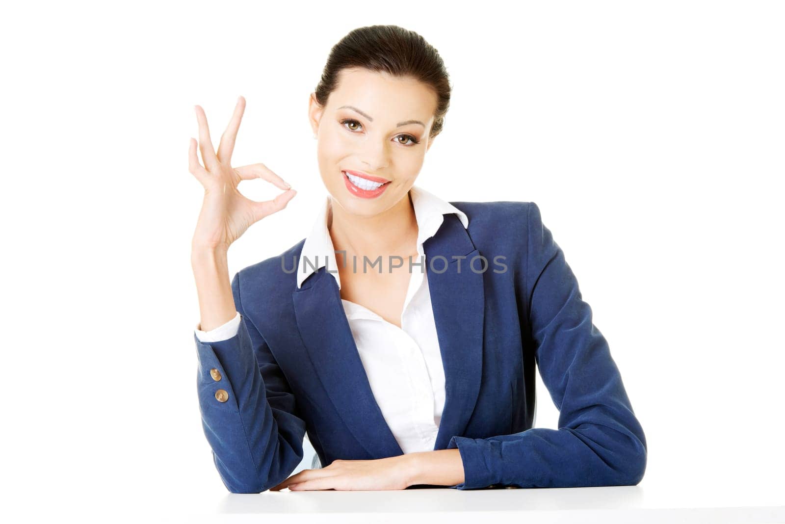 attractive business woman showing ok and sitting. isolated on white.