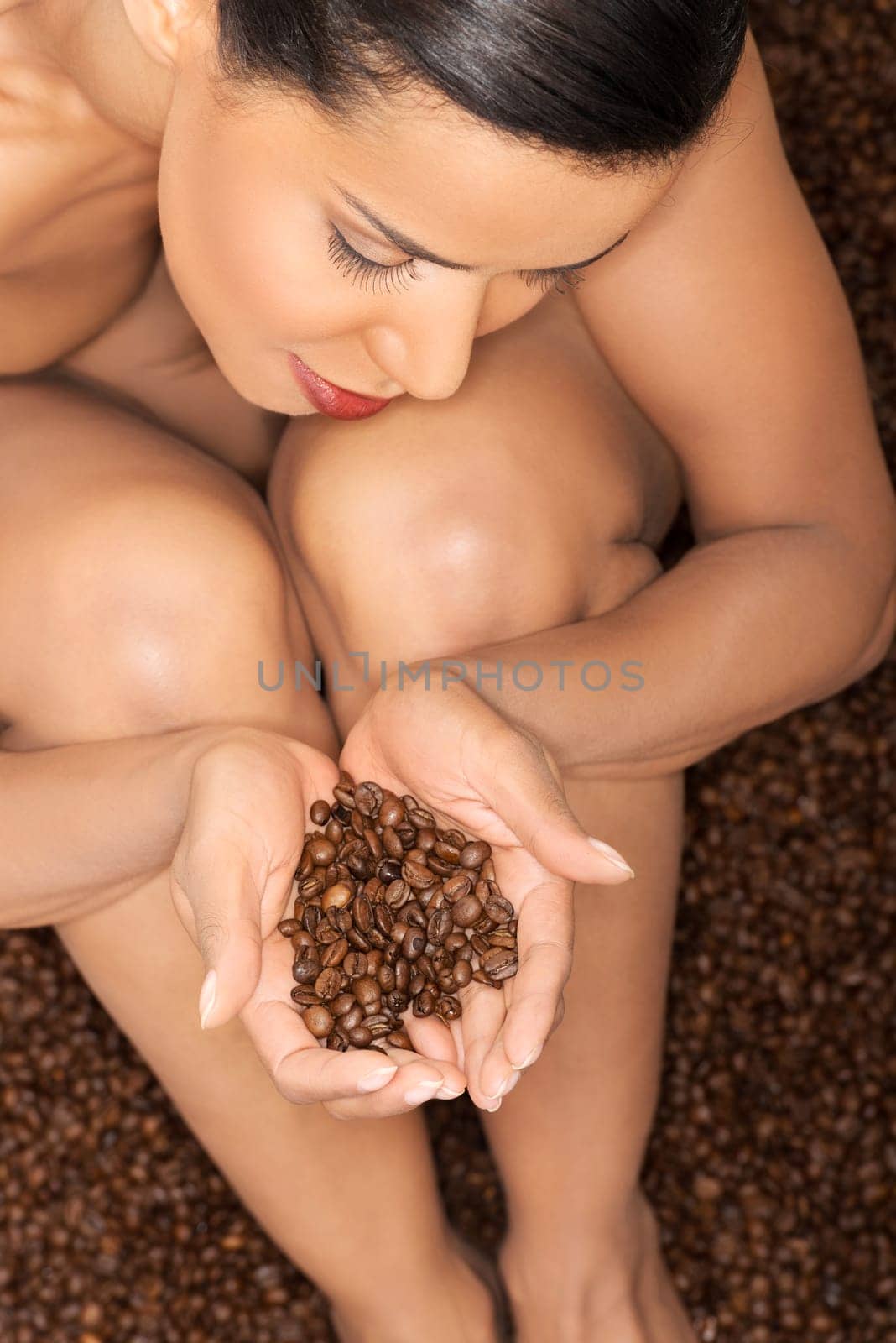 beautiful naked woman sitting in coffee seeds on them holding hands. up front view. closeup.