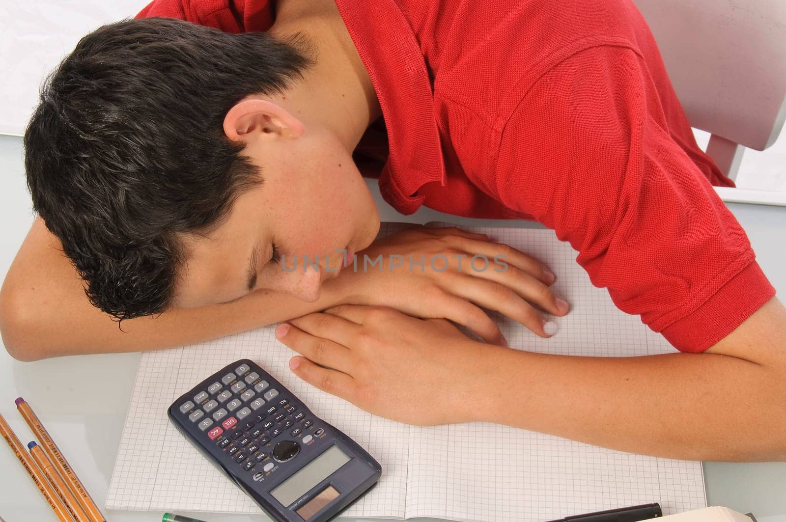 Boy sits exhausted and frustrated about homework at desk in front of a white background