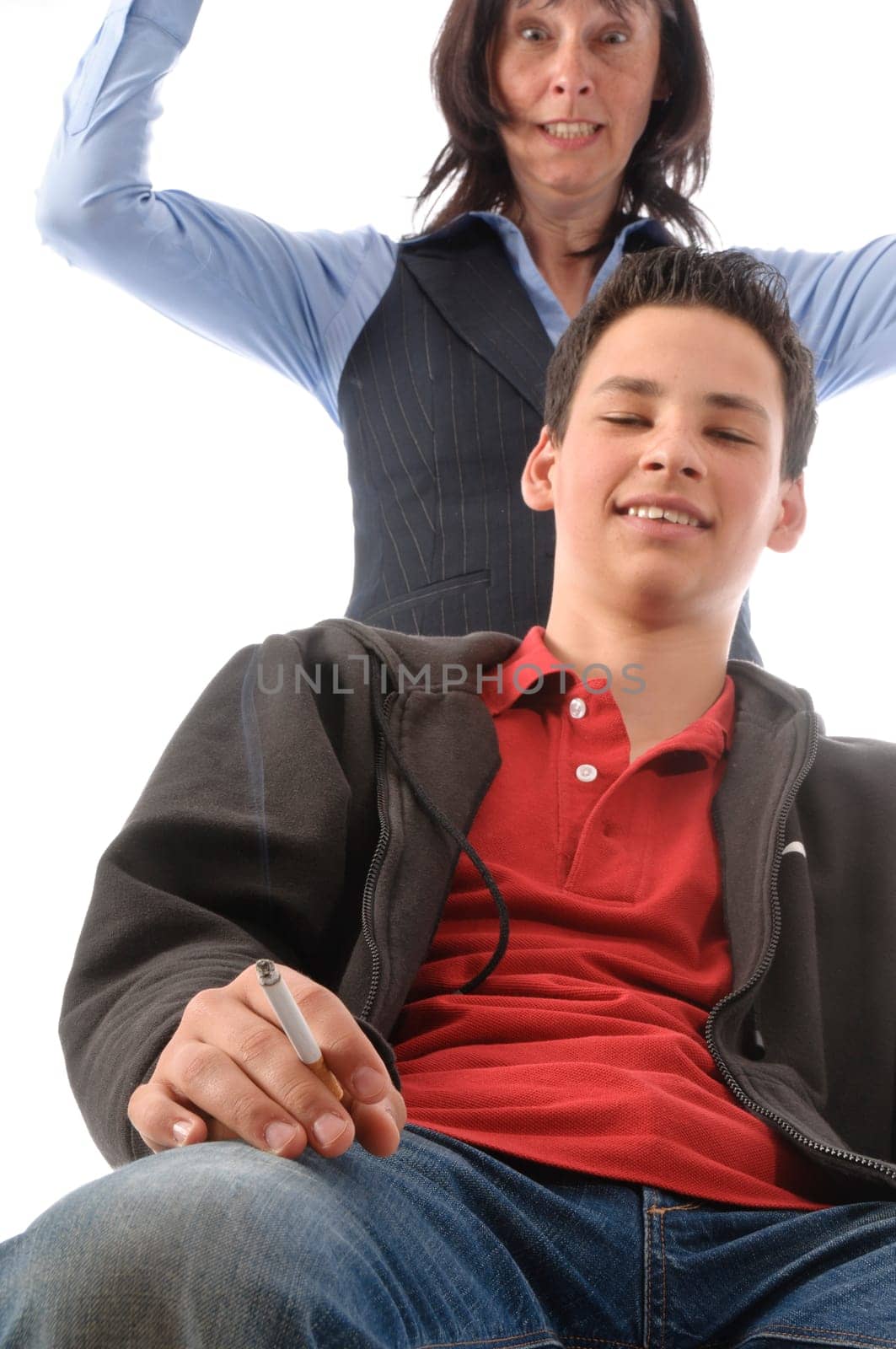 The boy sits casually in the room and smokes,the mother stands horrified behind it,in front of a white background.