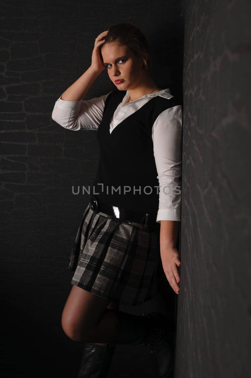 A young girl with blouse and boots stands in a dark corner of the room