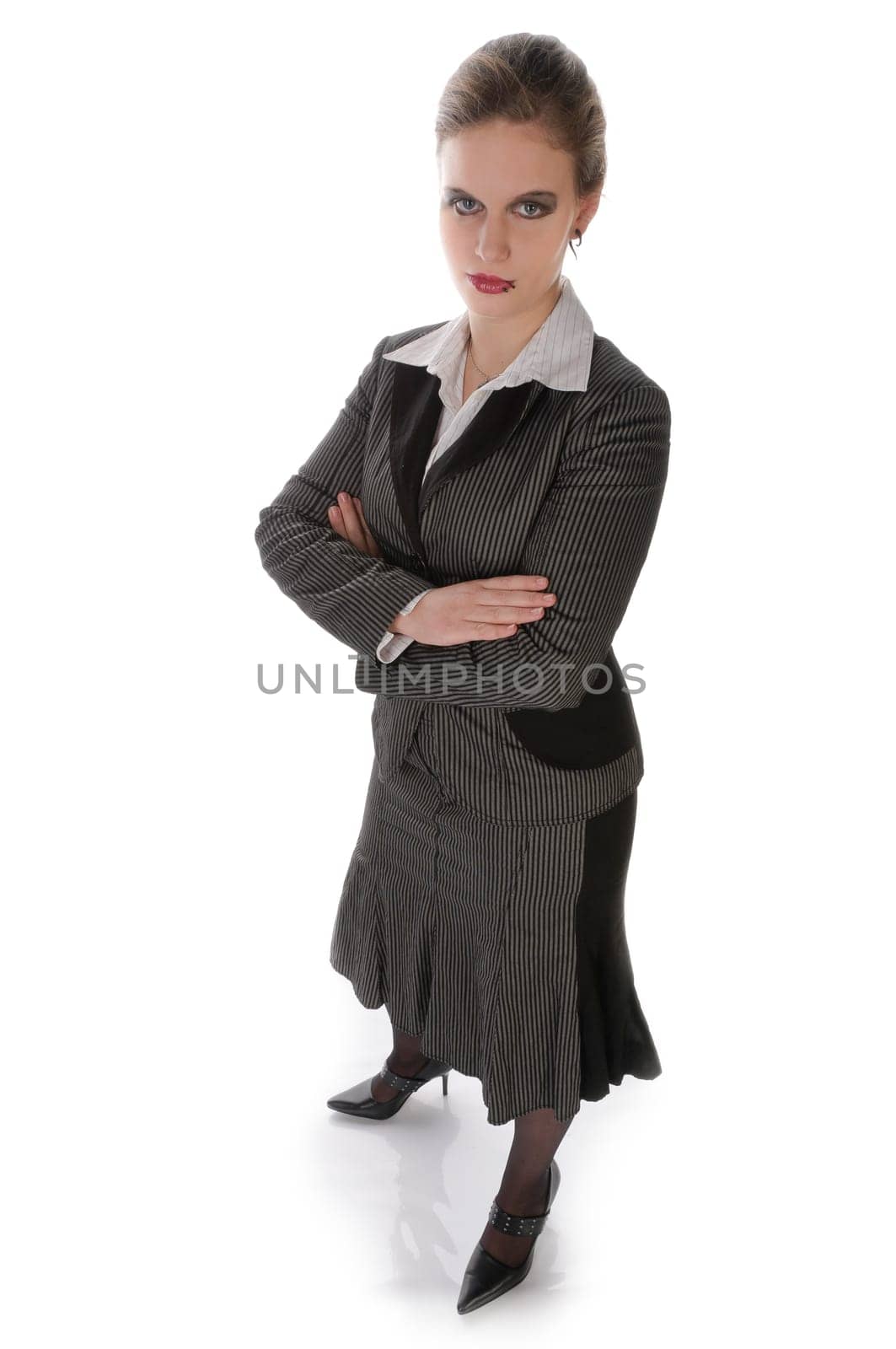 Young woman in grey business suit and high heels poses with folded arms against a white background