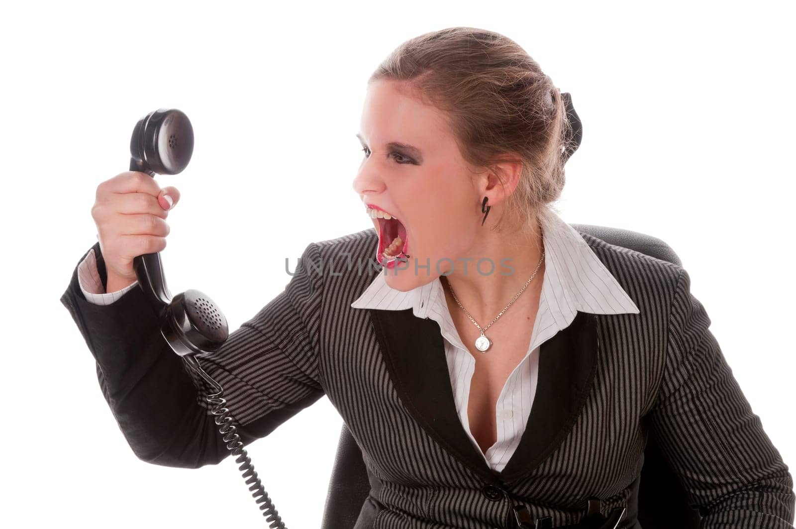 Young woman in grey business suit and high heels makes calls with landline telephone and yells angrily into the receiver against a white background