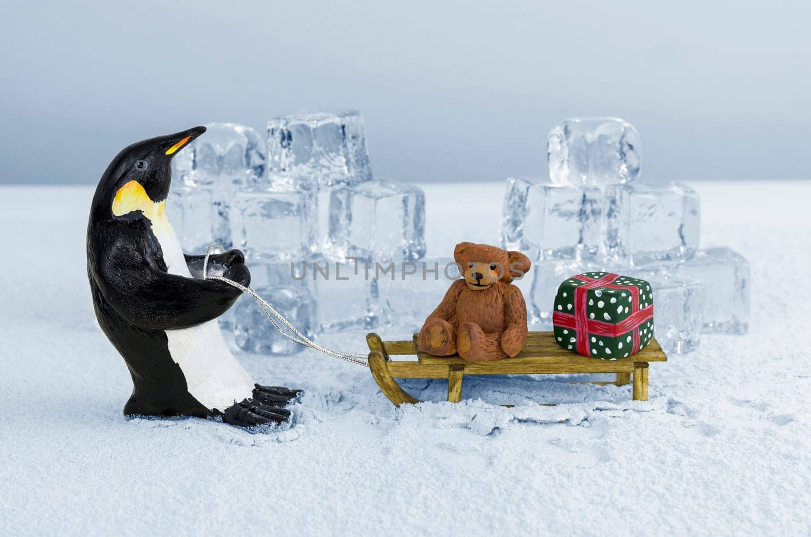 Penguin pulling sled with a teddy bear and a gift on board