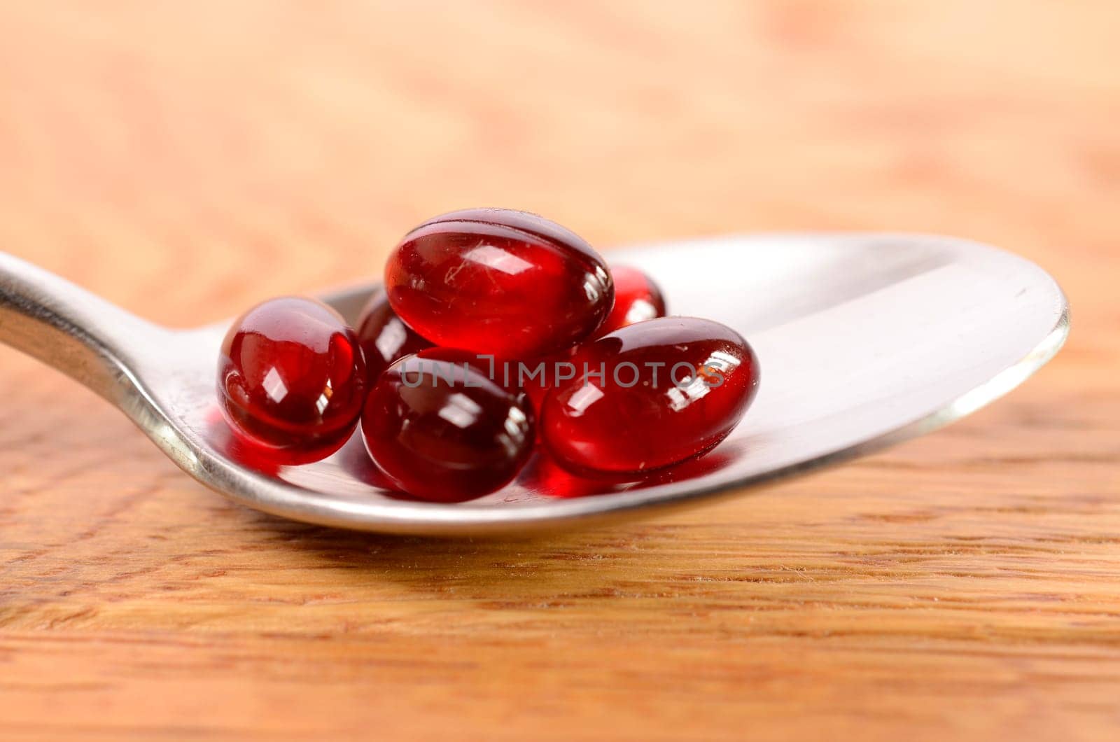 Red capsules on a spoon with a wooden background
