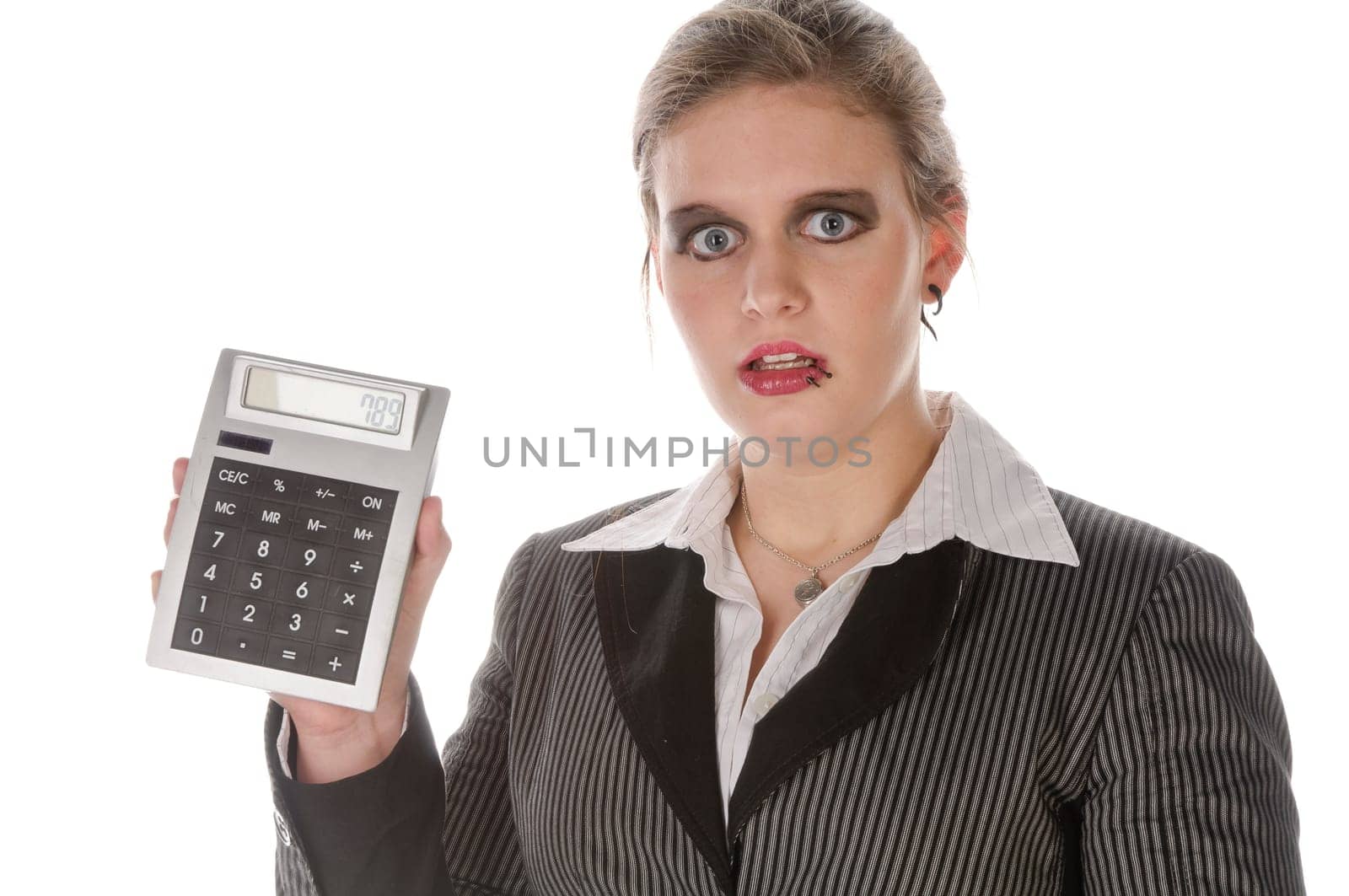 Young woman in a grey business suit and high heels looks horrified at her large calculator against a white background