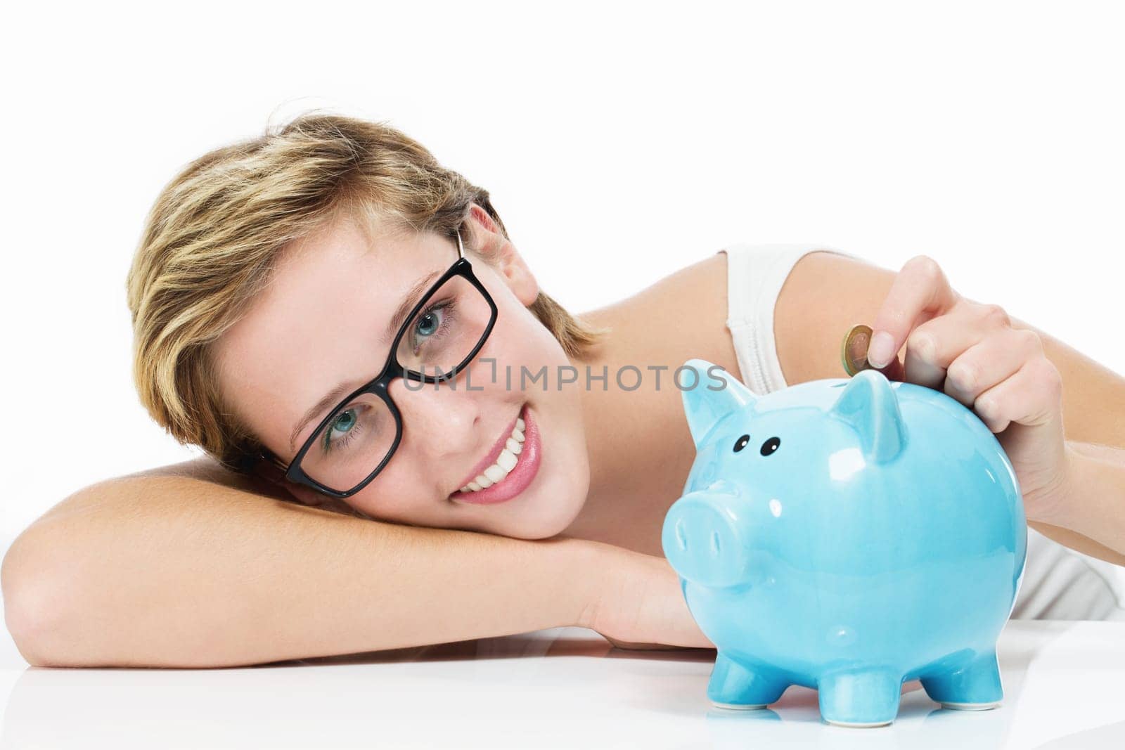 Happy woman tosses coin into her piggy bank on a white background