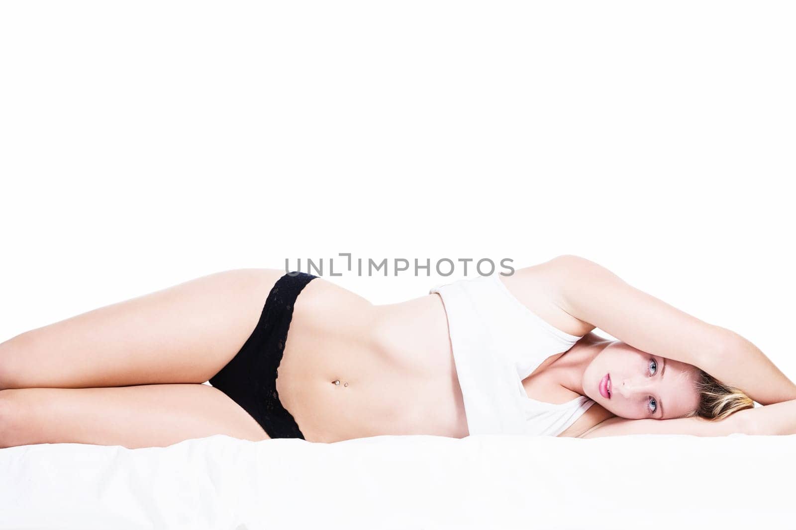 Young sensual woman lying sideways in bed on a white background