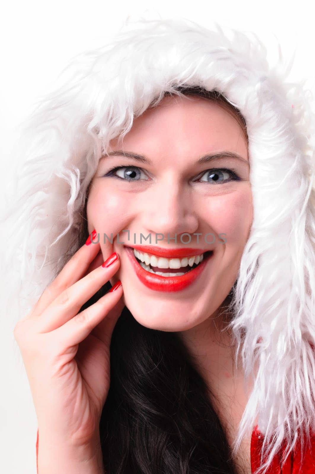 Portrait of an adult woman with long dark hair. She wears a red Christmas coat with a white fur collar and laughs into the camera,exposed against a white background.