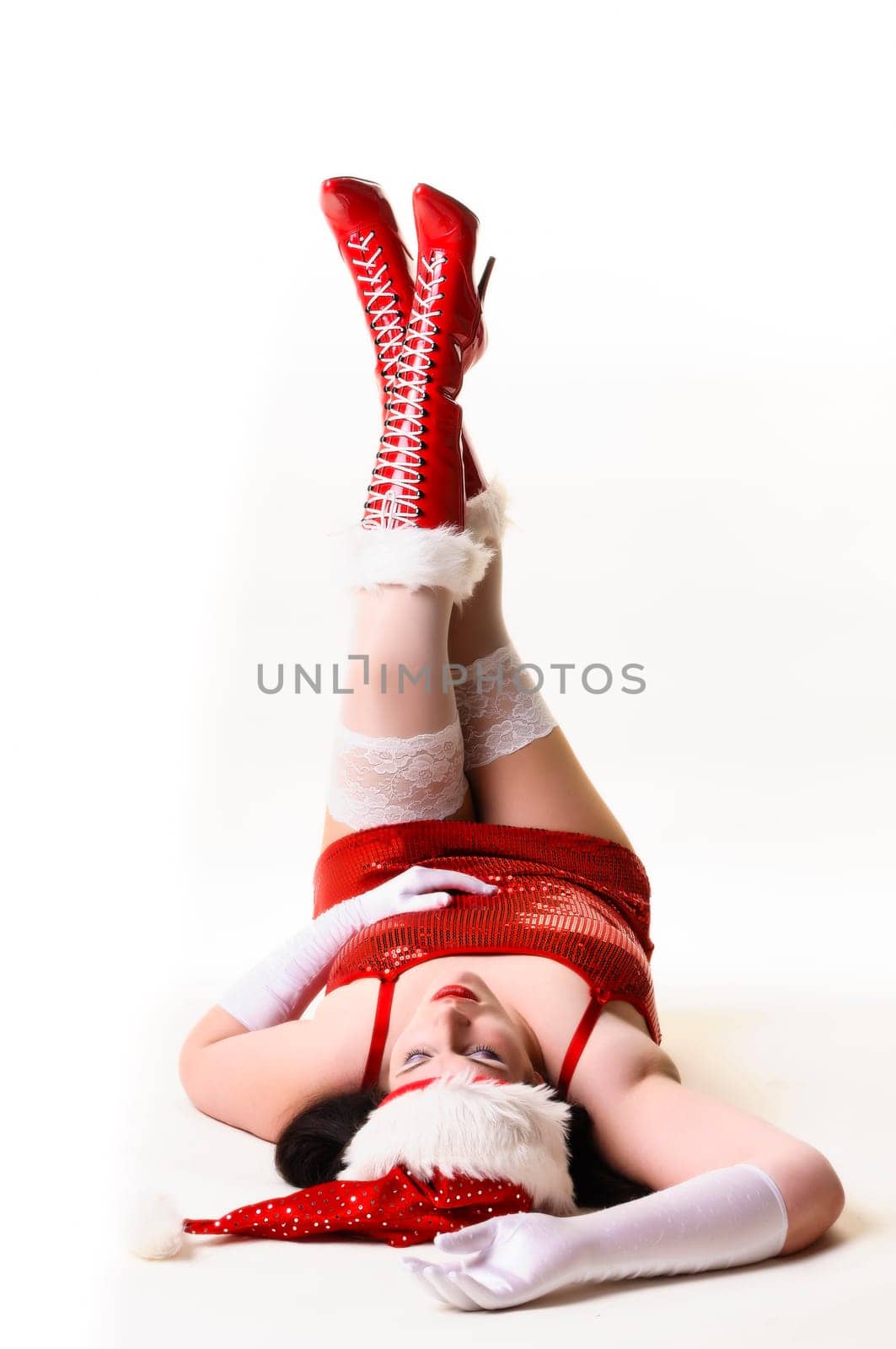 Sexy Santa Claus with red boots and Santa hat lies on the floor and stretches her legs upwards. Insulated against a white background.