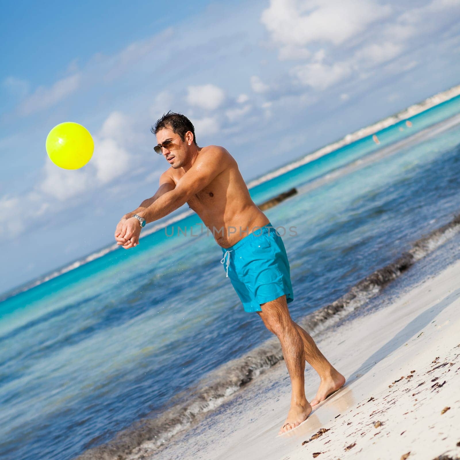 Young laughing man plays ball Football on the beach in summer holiday leisure