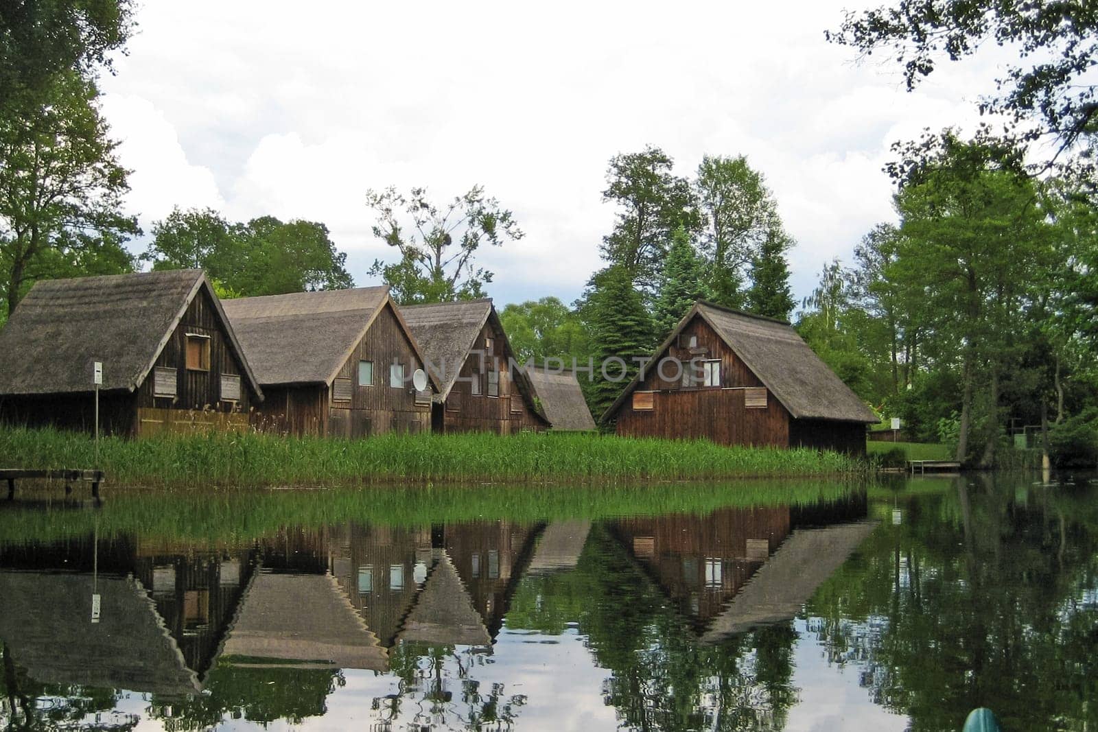 brown wooden boathouses reflecting in the water with reed and trees in the background