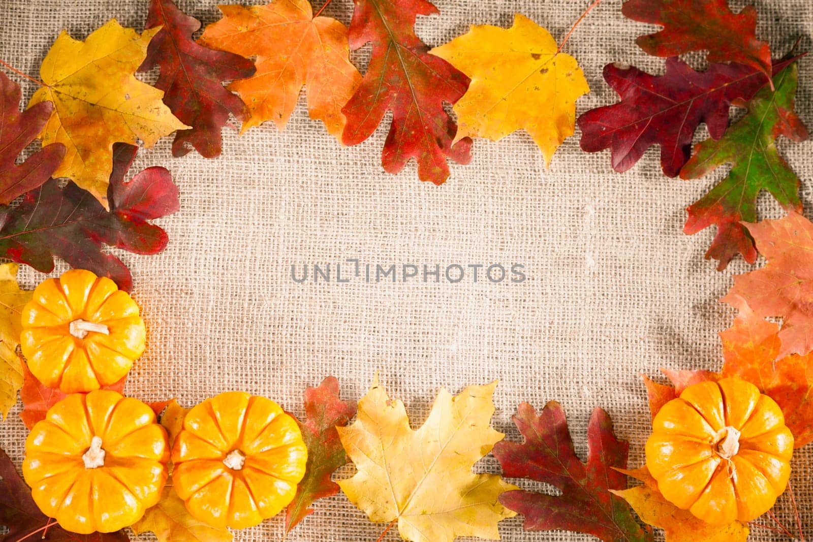 Fall-themed background of burlap, dry leaves and pumpkins