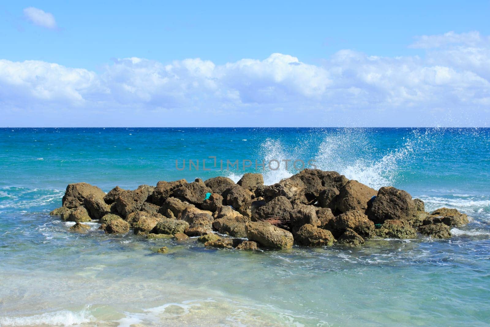 On a bright sunny day waves splash onto rocks on Deerfield Beach, Florida a beautiful scene and memorable because of it splendid beauty, unusualness and energy with its blue cloth washed ashore..
