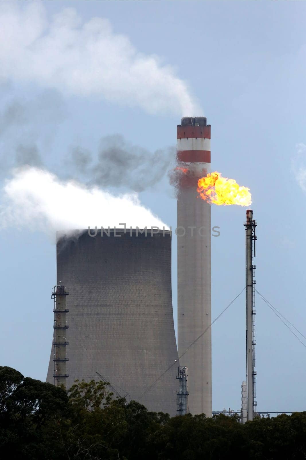 Energy production plant with cooling towers, chimneys and gas flame
