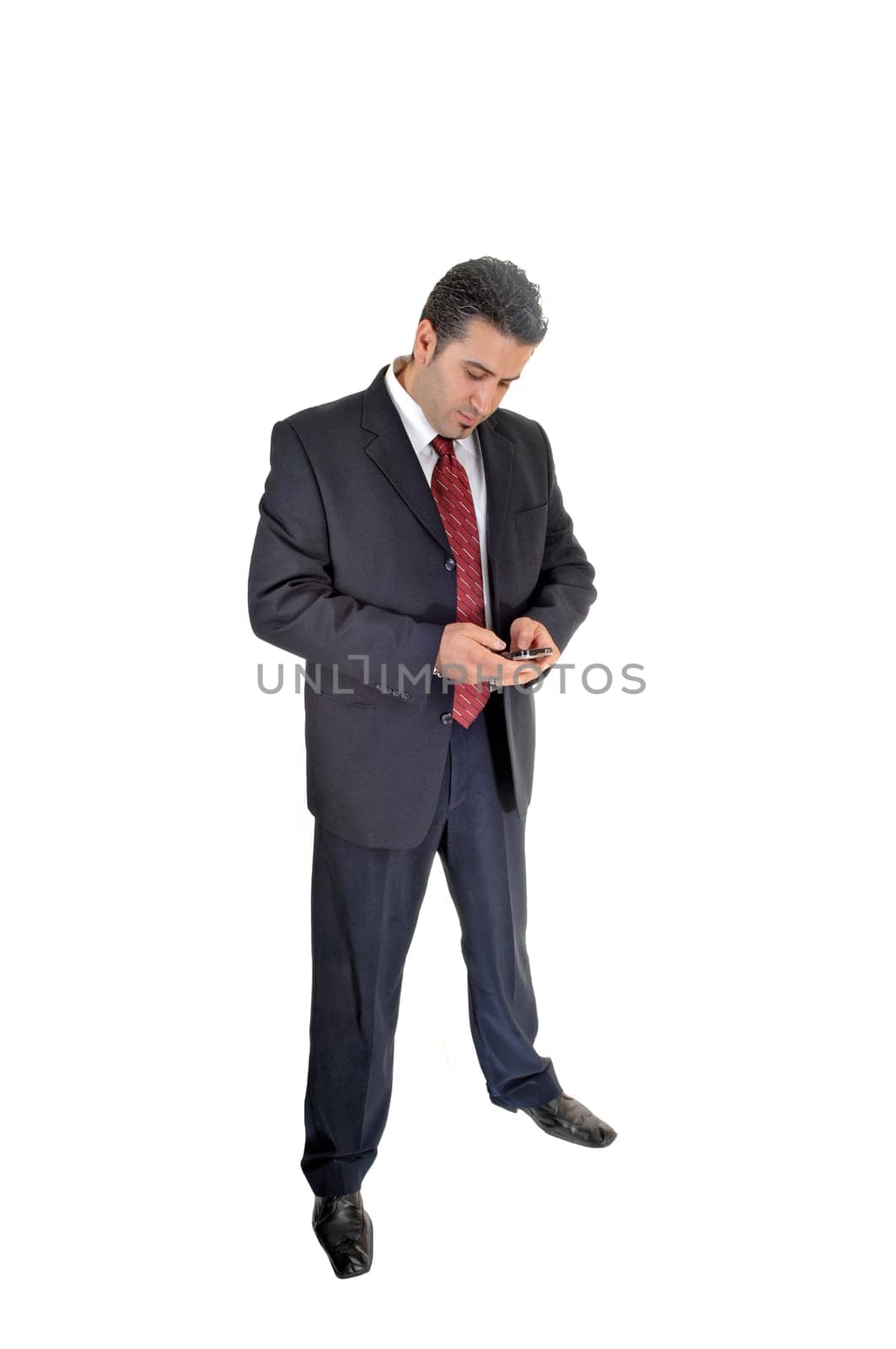 A tall handsome businessman standing for white background in a blue .suit dialling on his cell phone..