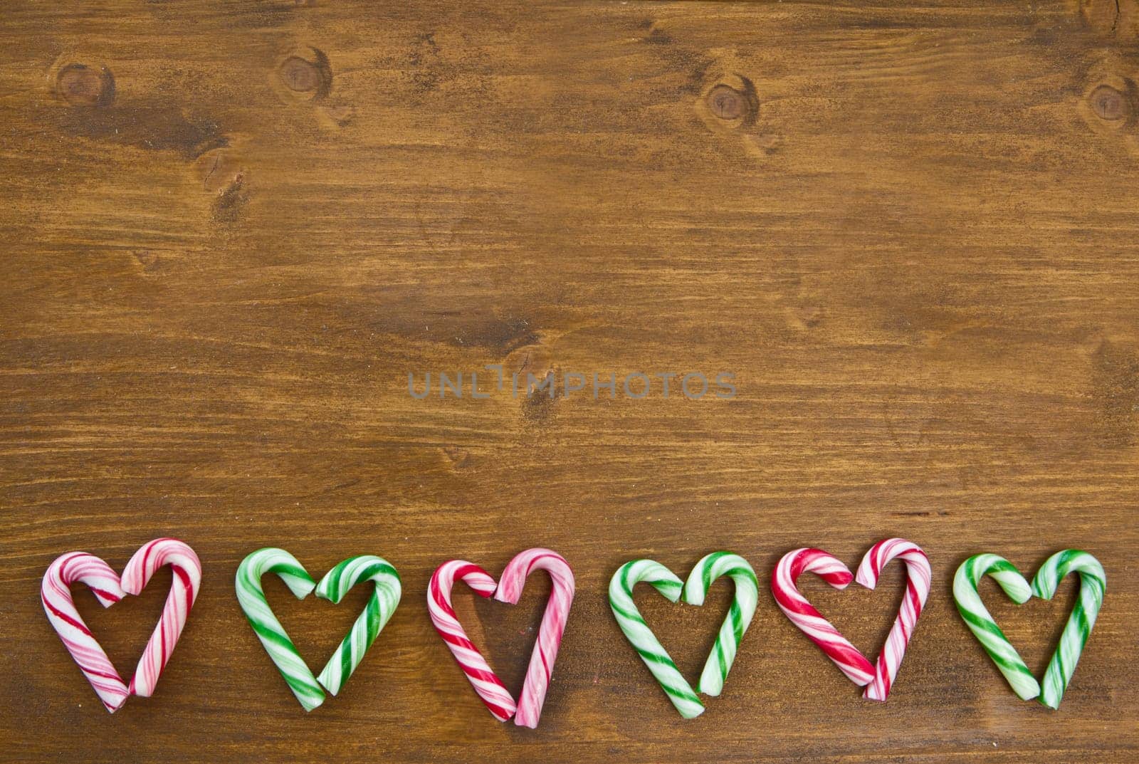 Colorful candy canes in heart shape on wooden background