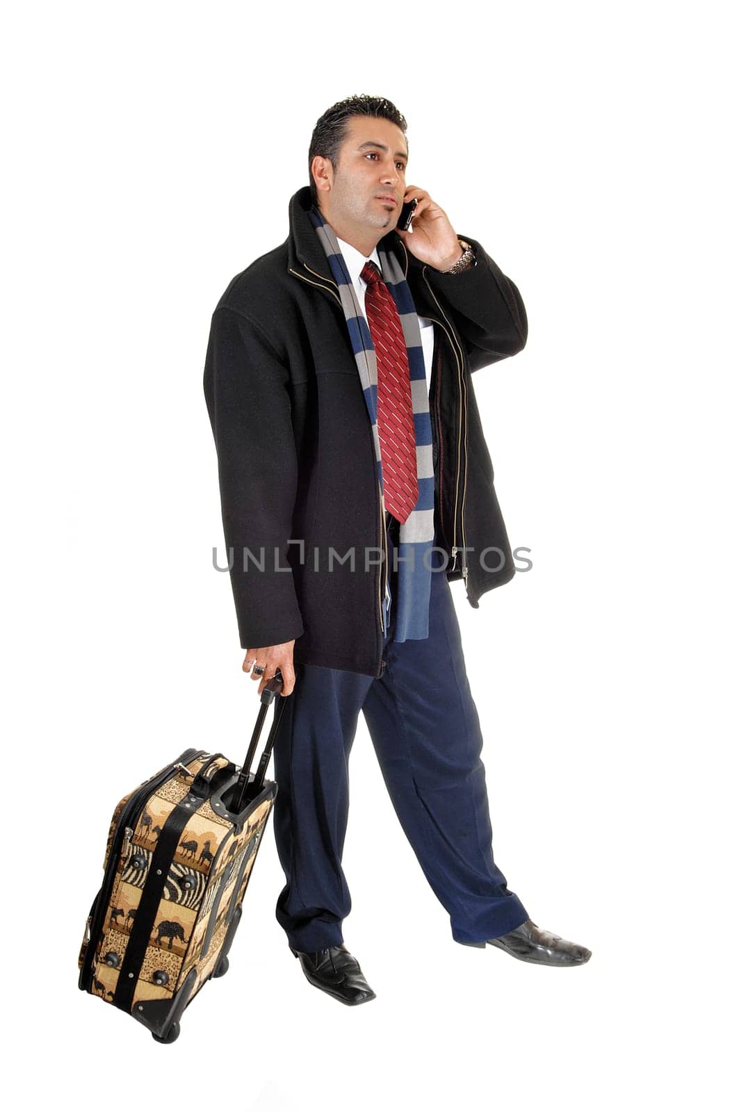 A handsome tall young businessman in a black coat with a .suitcase, talking on his cell phone, for white background...