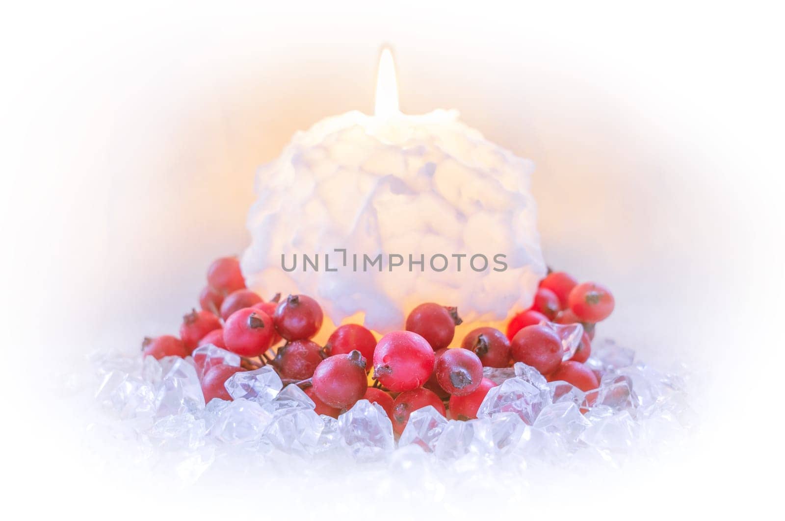Christmas candle in the shape of a snowball surrounded by red berries on ice