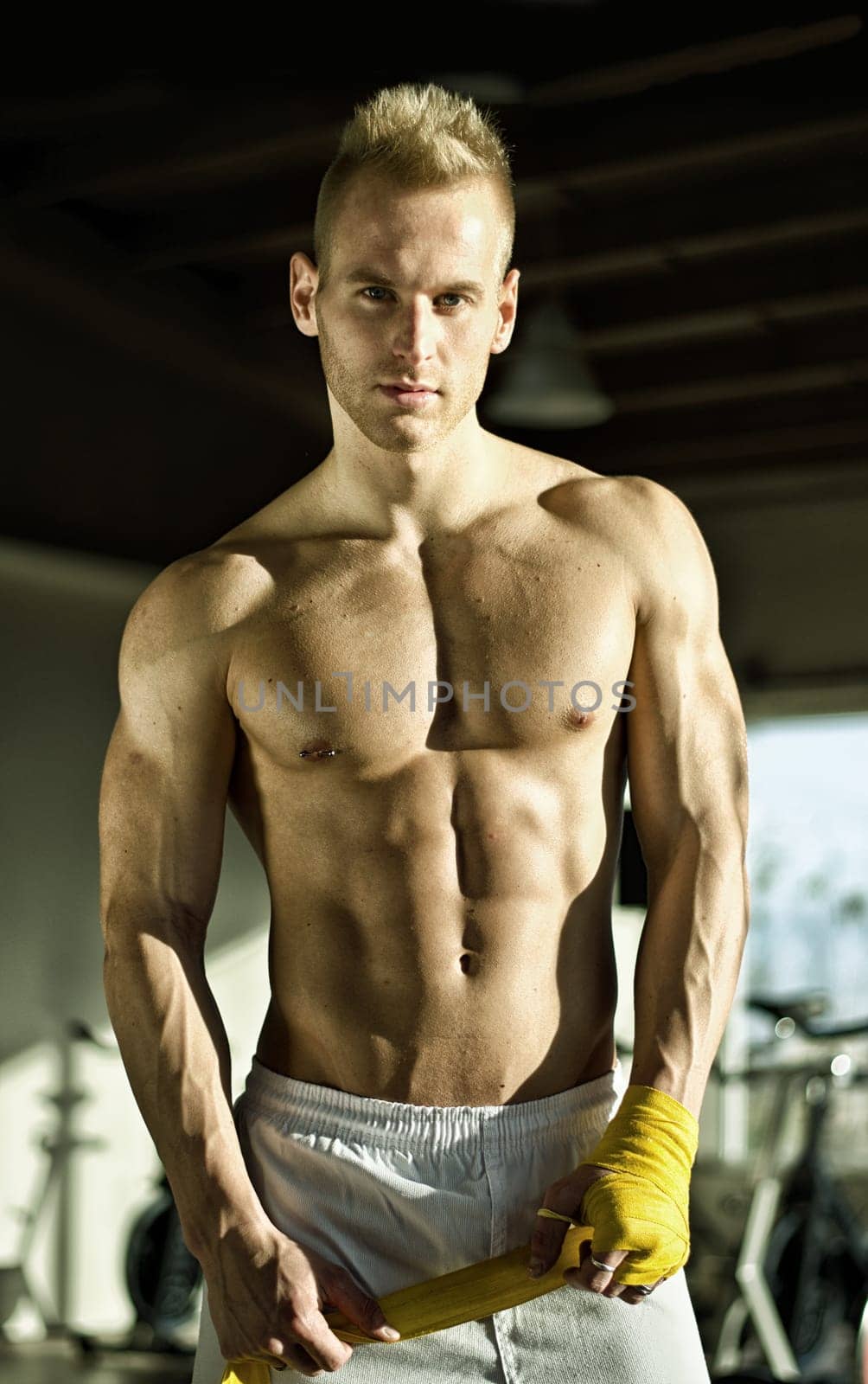 Muscular young man wrapping bandage around his hands for boxing