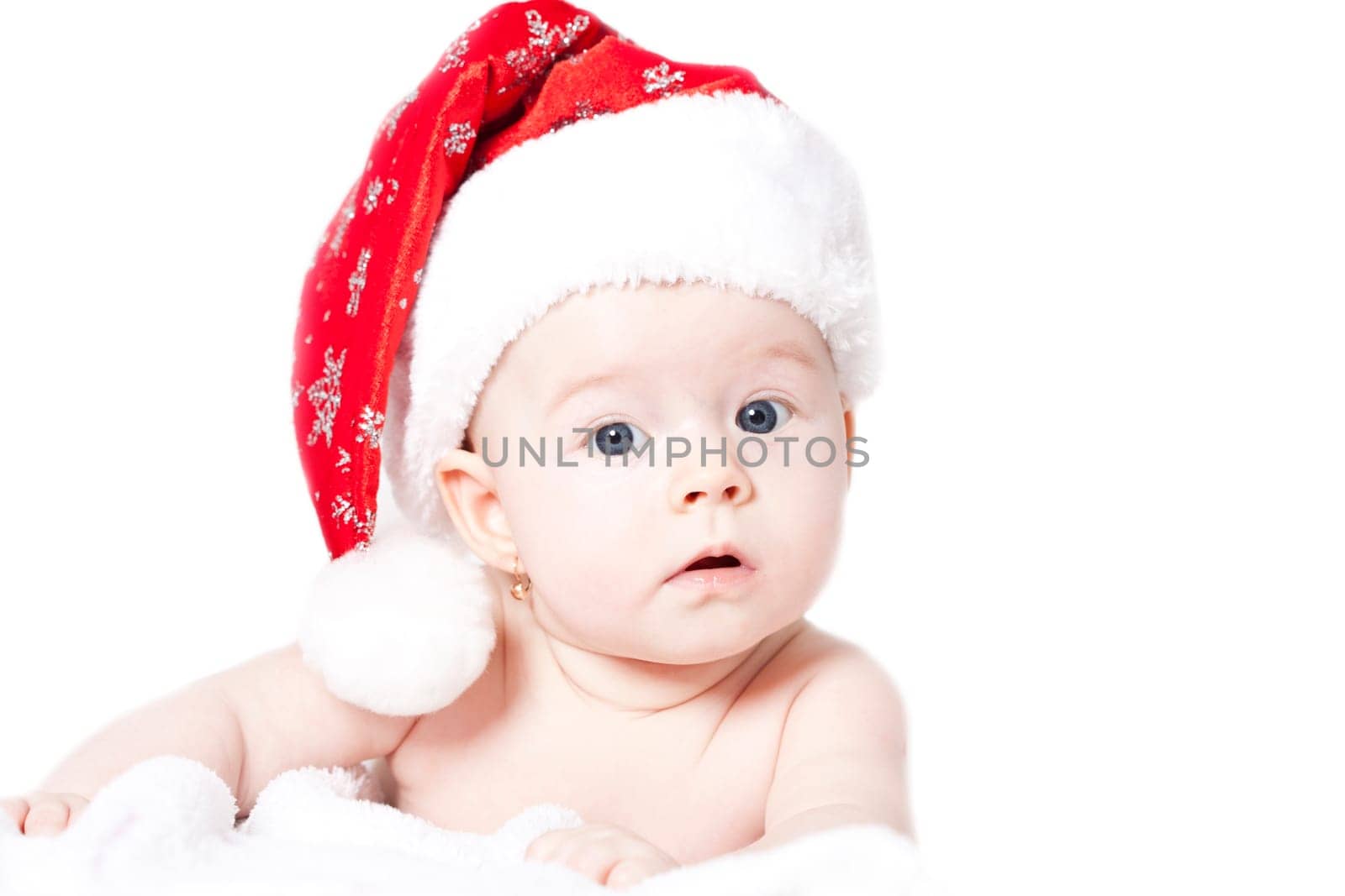 Baby girl lying on bed wearing red Santa hat