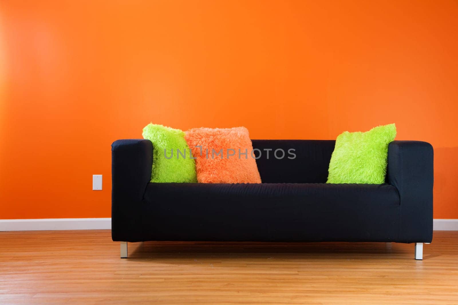 Contemporary black couch against bright orange wall in a modern living room