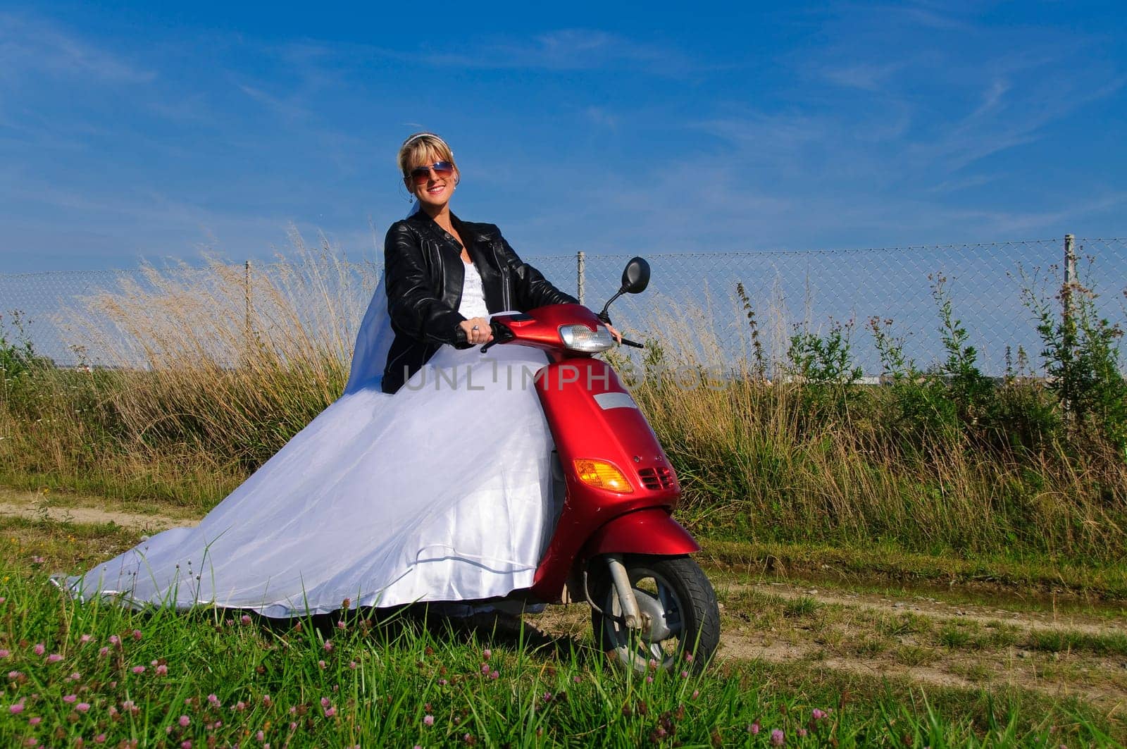 Bride in white wedding dress rides on a moped to the wedding ceremony