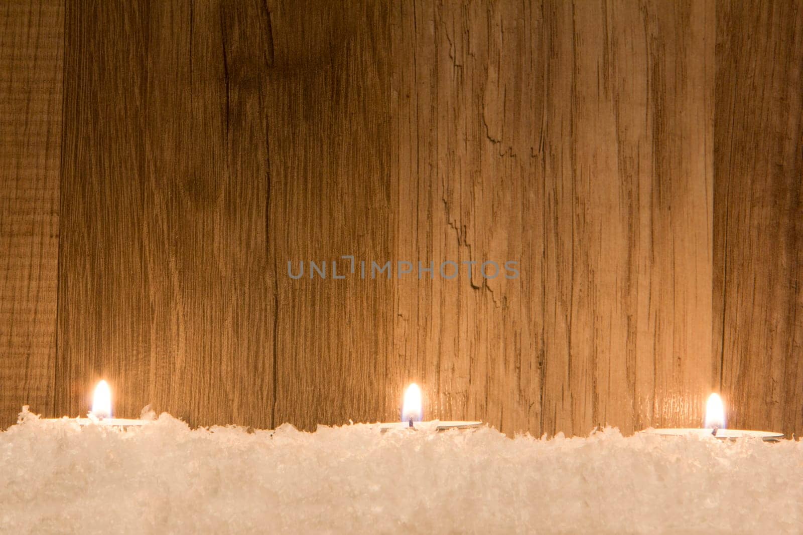 several candles in the snow with wooden background