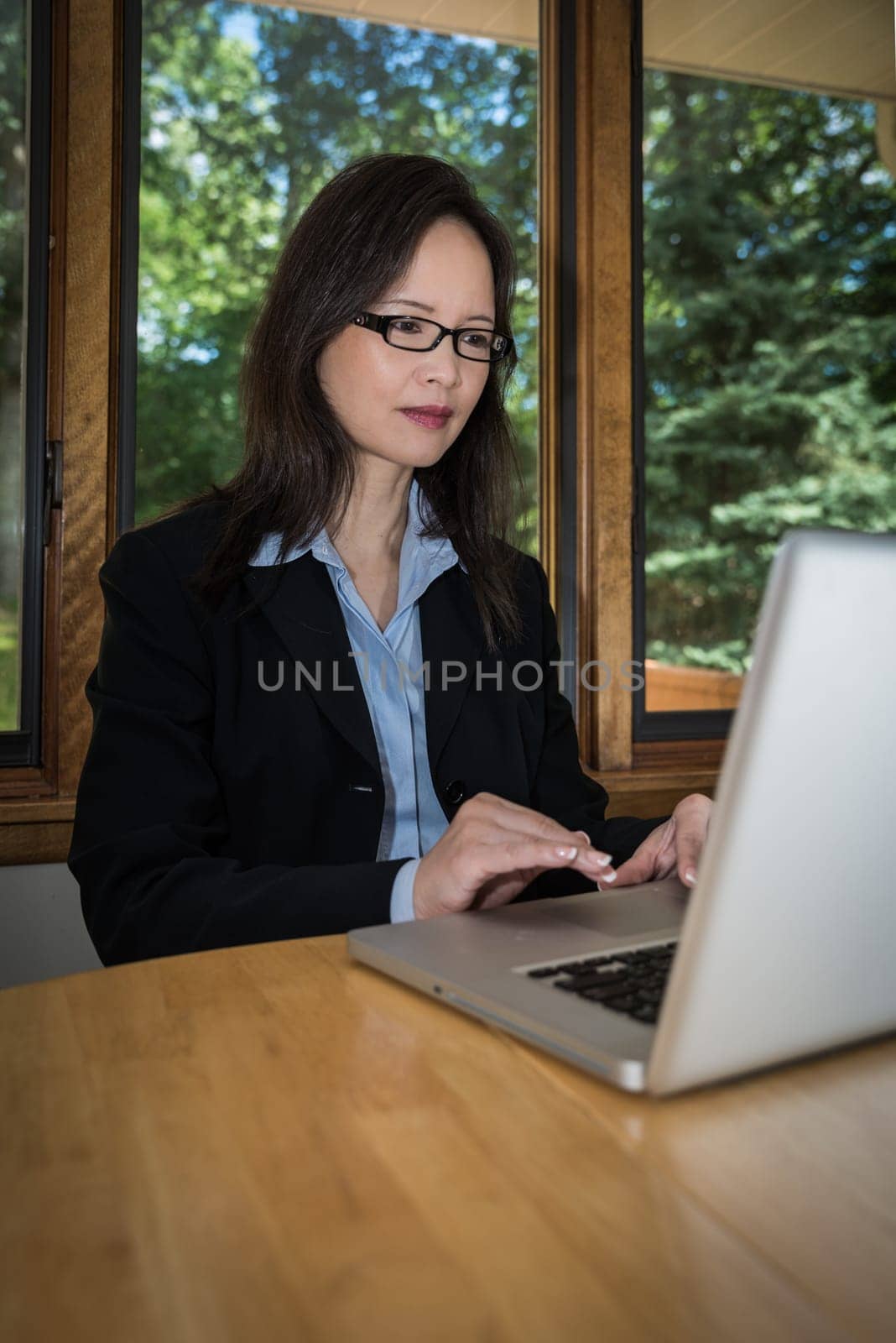 Woman in business suit with laptop on desk typing and searching in front of a window