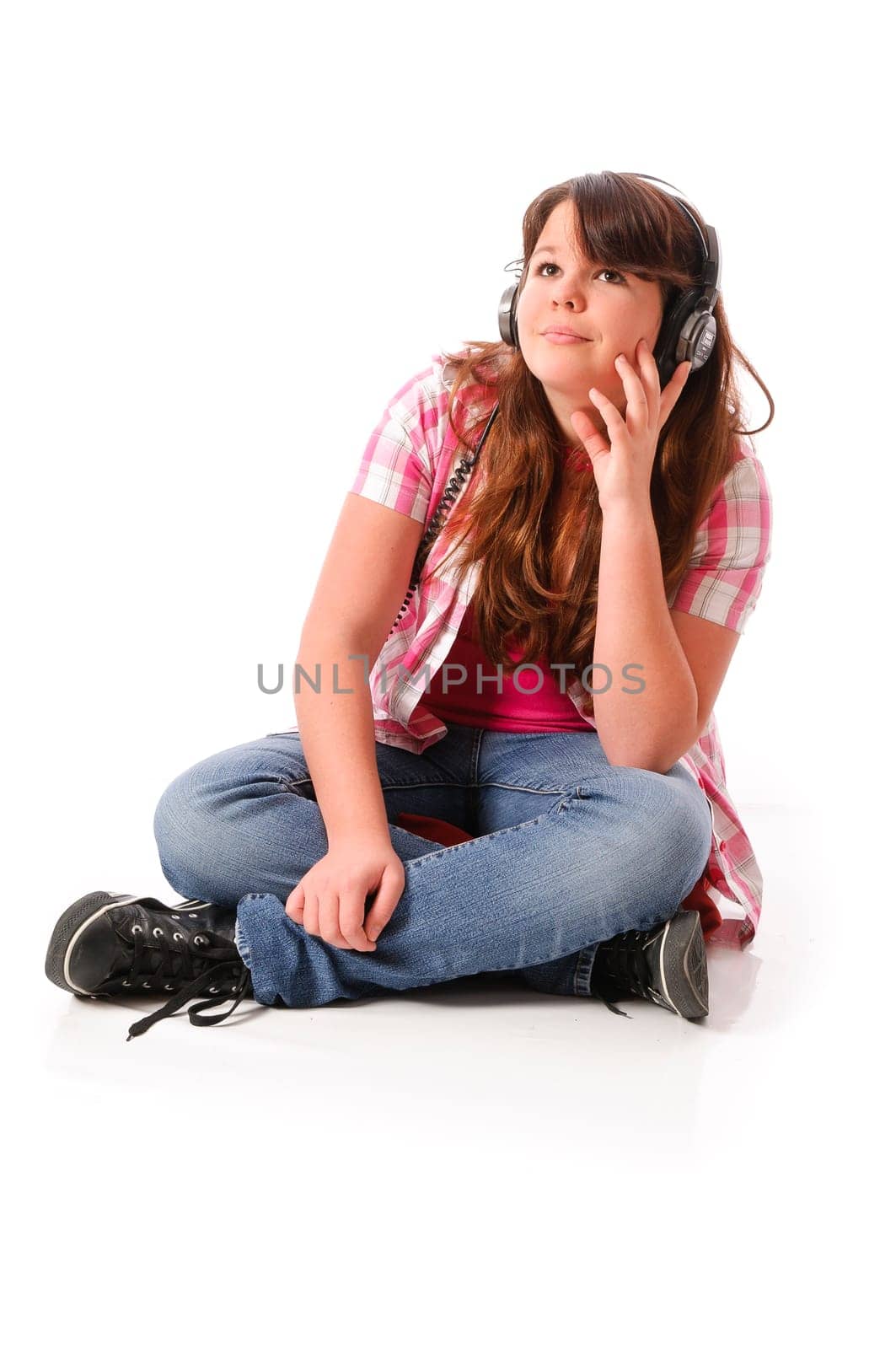 Young mGirl with long dark hair listens enthusiastically to music with headphones against a white background.