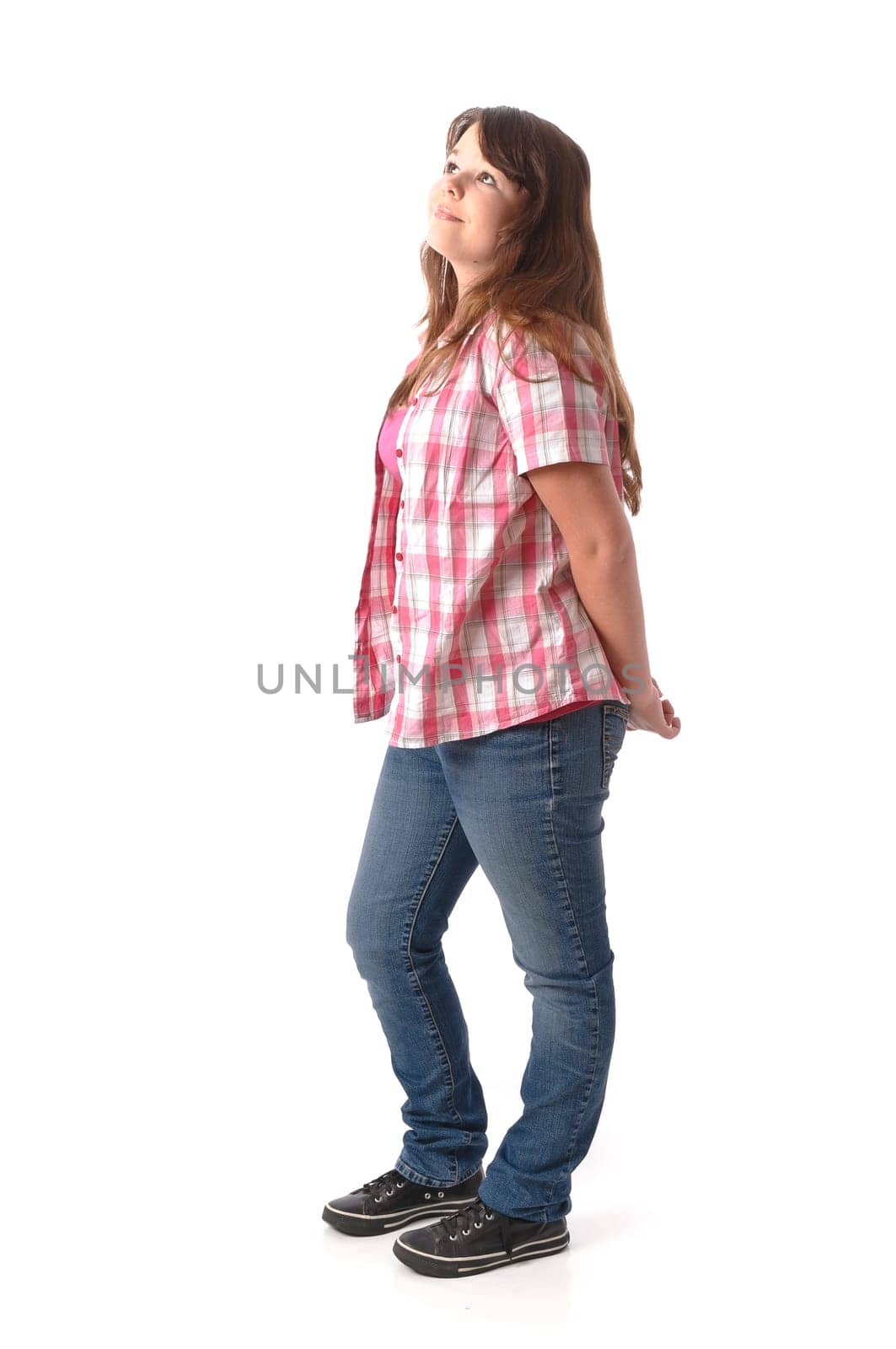Girl with long dark hair wears a checkered blouse and jeans,stands in front of a white background
