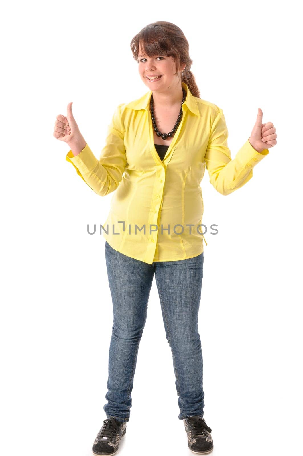 Pretty teenage girl in yellow blouse and jeans poses against a white background. Make 'thumbs up' gesture and laugh.