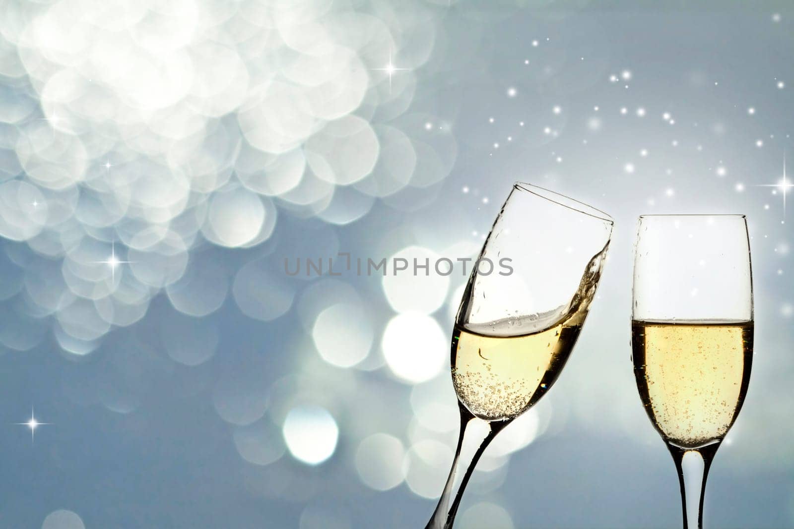 Glasses with champagne against holiday light and snowflakes