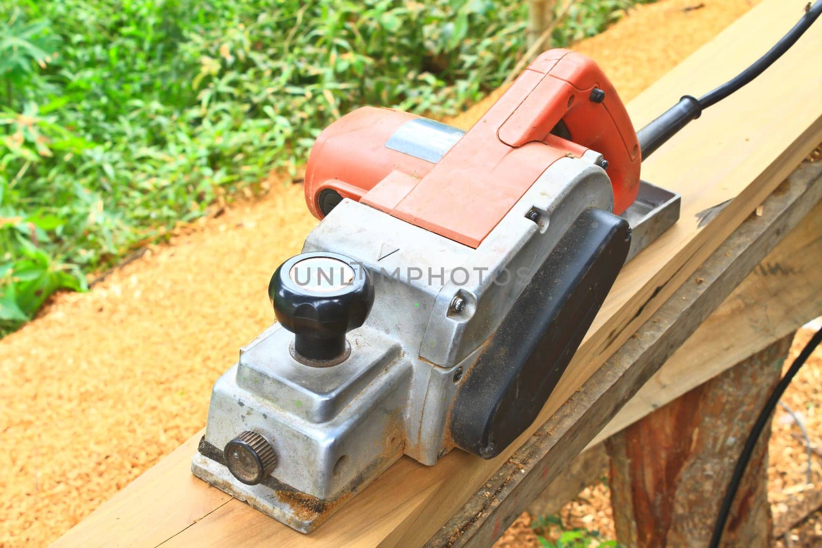 Close up construction worker's hand and power tool while planing a piece of wood trim for a project