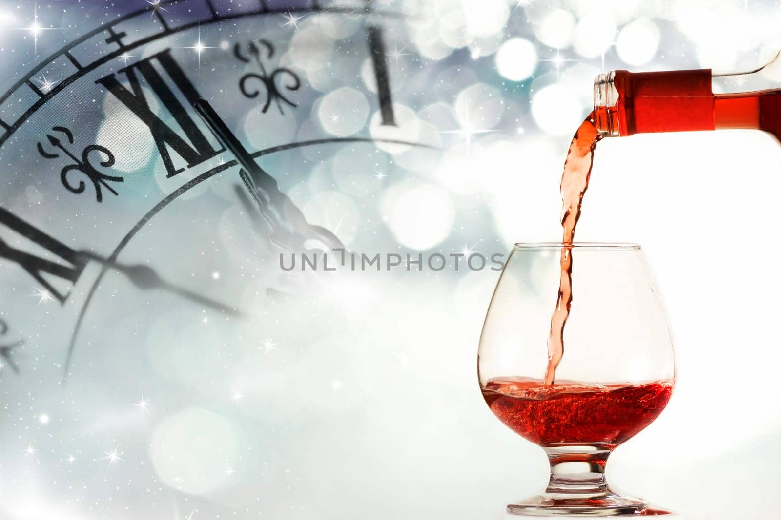 Glasses of wine against clock close to midnight and holiday lights