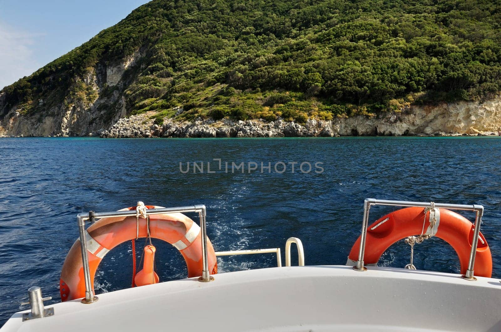 Boat stern with life buoys. Distant island, blue sea and rocky coast.