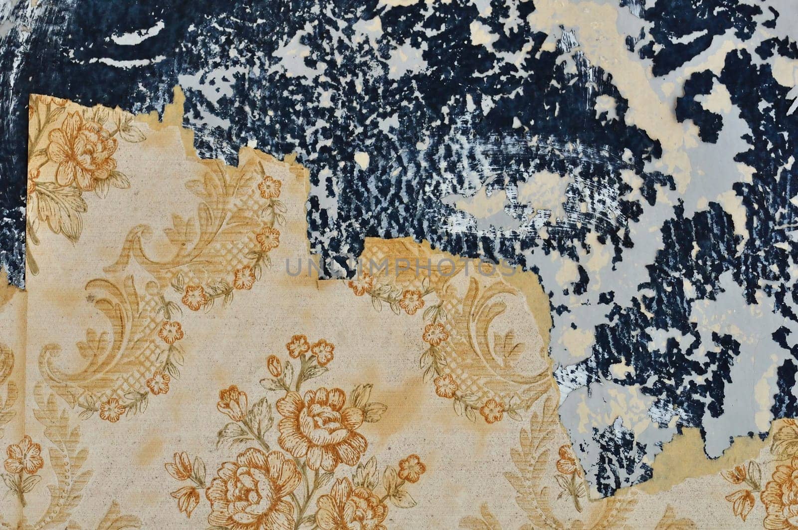 Torn floral pattern wallpaper on peeling paint wall. Grungy background.